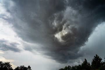 Dangerously broiling thundercloud with a twister vortex forming over some treetops