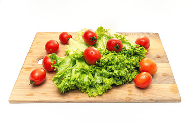 Bright red cherry tomatoes and green lettuce on a wooden board. Vegan food. Salad preparation.