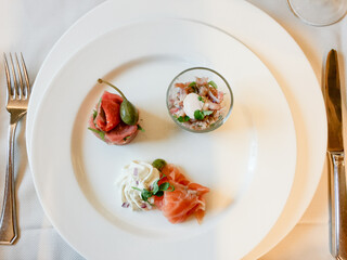This image exemplifies the elegance of gourmet cuisine with a minimalist presentation. Three small, artfully arranged starters are placed on a large white plate, which emphasizes their vibrant colors
