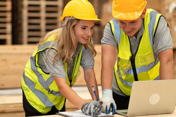 Caucasian businesswoman and man holding clipboard and notebook computer with stock timber background at wood factory
