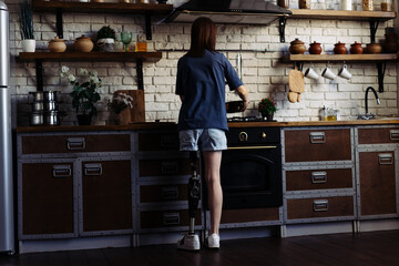 Female with prosthetic leg puts pot on stove to prepare food