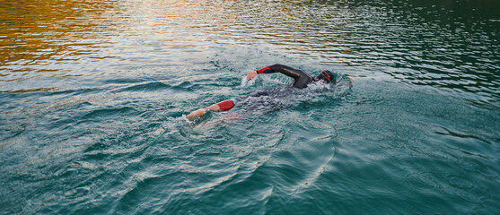 Triathlon athlete swimming on lake in sunrise wearing wetsuit