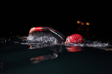 A determined professional triathlete undergoes rigorous night time training in cold waters,...