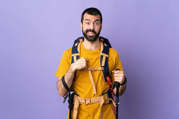 Caucasian handsome man with backpack and trekking poles over isolated background pointing to oneself