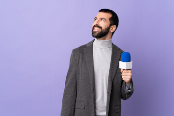 Naklejka premium Adult reporter man with beard holding a microphone over isolated purple background thinking an idea while looking up