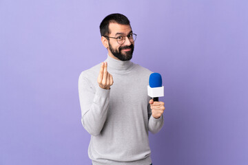 Adult reporter man with beard holding a microphone over isolated purple background making money...