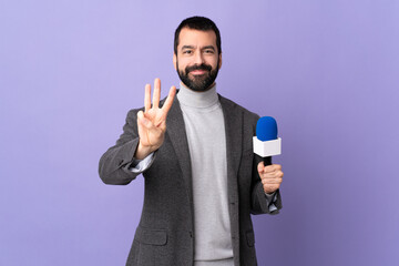 Adult reporter man with beard holding a microphone over isolated purple background happy and...