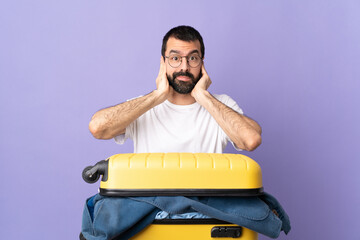 Traveler caucasian man with a suitcase full of clothes over isolated purple background frustrated...