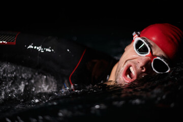 A determined professional triathlete undergoes rigorous night time training in cold waters,...