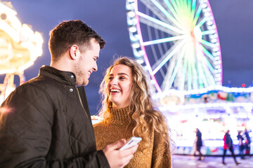 Happy couple at amusement park looking at mobile phone and laughing