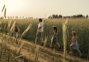 The girls run with their dad in a race along a dirt road in a field near the rye