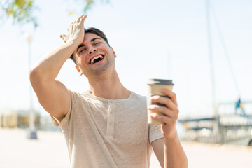 Young handsome man holding a take away coffee at outdoors has realized something and intending the solution - obrazy, fototapety, plakaty