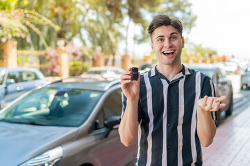 Young handsome man holding car keys at outdoors with shocked facial expression