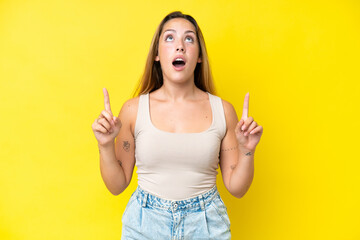 Young caucasian woman isolated on yellow background surprised and pointing up