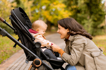 Young woman with cute baby girl in baby stroller at the autumn park