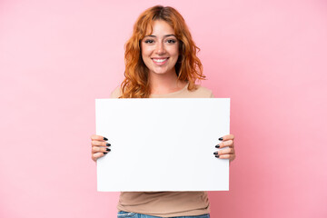 Young caucasian woman isolated on pink background holding an empty placard with happy expression