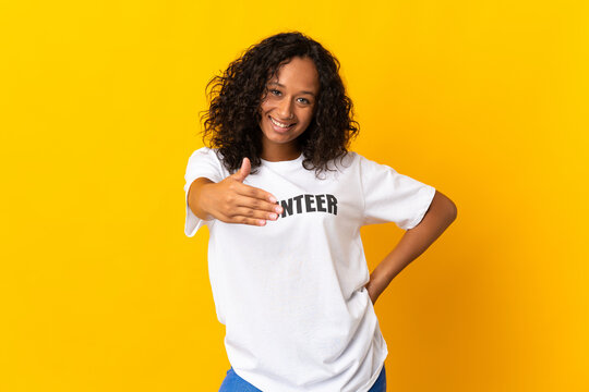 Teenager cuban volunteer girl isolated on yellow background shaking hands for closing a good deal