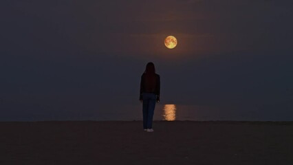 Moving shot of woman silhouette looking at the full moon light reflection on the surface of the water on the beach - Powered by Adobe