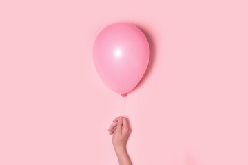 Pastel pink balloon with female hand on pink background. Lightness concept.