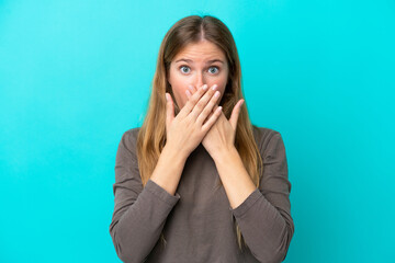 Young blonde woman isolated on blue background covering mouth with hands
