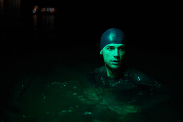 Authentic triathlete swimmer having a break during hard training on night neon gel light