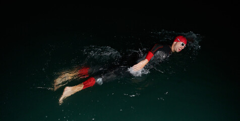 A determined professional triathlete undergoes rigorous night time training in cold waters,...