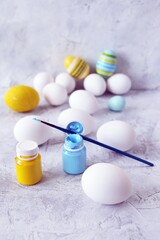 Easter eggs painted in pastel colors, yellow and blue paint, brushes on a concrete table