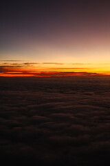 Sunset over the clouds. Beautiful orange color sky over a sea of clouds, view from the airplane window. Flying through the clouds, amazing nature landscape.