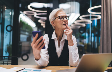 Thoughtful senior businesswoman using smartphone in meeting room