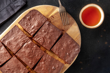 Chocolate brownie with tea, coffee cake, overhead flat lay view on a black background, with copy space