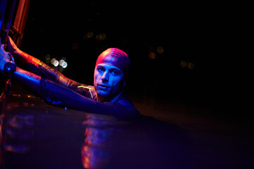 authentic triathlete swimmer having a break during hard training on night neon gel light