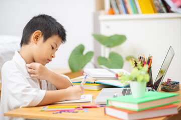 Asian Boy Doing homework with the intention. Child boy holding pencil writing, A boy drawing on white paper at the table,Elementary school and home schooling, Distance Education concept.