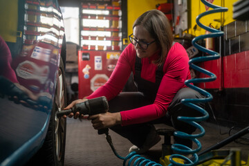 Portrait confident female auto mechanic working in garage. Female mechanic adjusting the tire at...