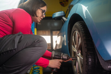Technician woman working in auto repair workshop. Portrait confident female auto mechanic working in garage. Female mechanic adjusting the tire at repair garage alone, in overalls uniform. 