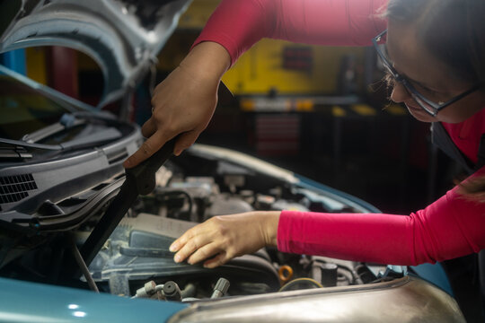 Female auto mechanic inspecting a car under the hood. Smiling  mechanic checking and maintenance car engine or vehicle with herself. Copy space. 