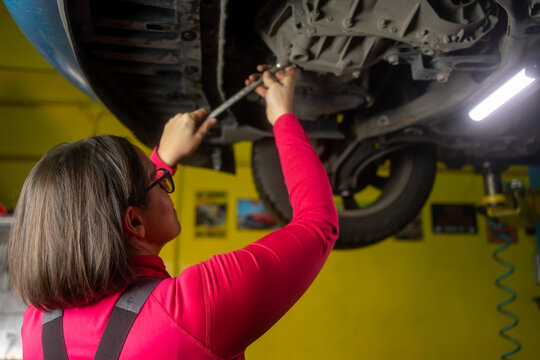 Shot of a Female Mechanic Working Under Vehicle in a Car Service. Empowering Woman Wearing Gloves and Using a Ratchet Underneath the Car. Modern Clean Workshop.