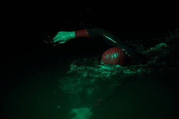 Authentic triathlete swimmer having a break during hard training on night neon gel light