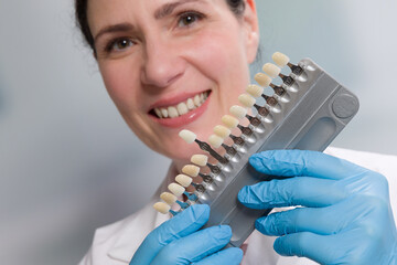 dentist's assistant / female dentist with medical gloves holds/shows shade guide to check veneer of teeth