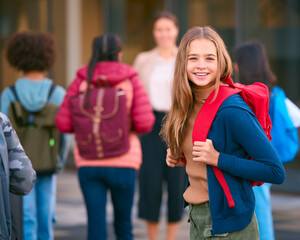Obraz premium Portrait Of Female Secondary Or High School Student Outside School Building With Teachers And Pupils
