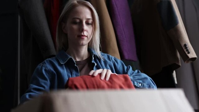 woman sorts things into cardboard box at home to give to charity or recycling, Poland