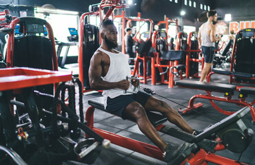 Black man perform exercise with machine in gym of modern fitness center