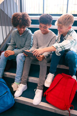 Three Male Secondary Or High School Pupils Inside School Building On Stairs With Digital Tablet