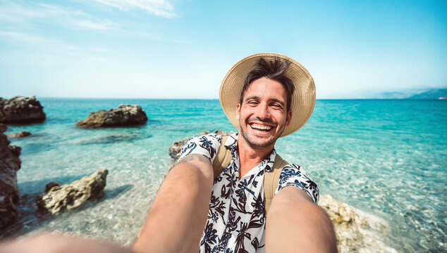 Happy man taking selfie with smart mobile phone outside - Cheerful tourist enjoying summer vacation at the beach - Travel life style and technology concept