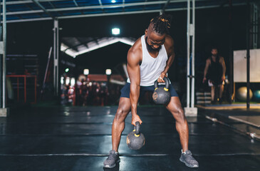 Fototapeta na wymiar Strong black male athlete lifting kettlebells during workout in gym
