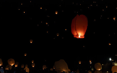orange flaming Chinese lanterns floating in the air. people filming with their cell phones