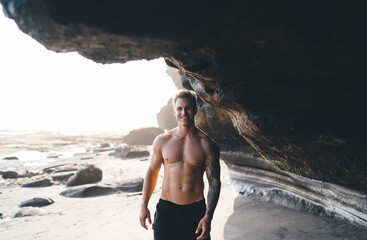 Shirtless man standing under rock on sandy beach