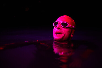 Authentic triathlete swimmer having a break during hard training on night neon gel light