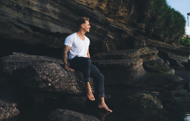 Happy man sitting on stone near water in rocky cliff