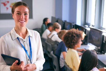 Portrait Of Female Secondary Or High School Teacher With Students At Computers In IT Class