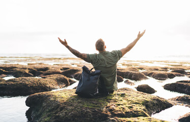 Unrecognizable man admiring view of sea water while sitting on rocky shore